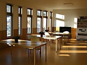 大きな窓がたくさん付いた談話コーナー。奥には自動販売機が置かれ、窓際にはテーブルが設置されている。