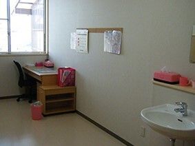 車いす対応の洗面所が設置された部屋にはデスクセットが置かれ、小さな収納ケースやゴミ箱がある。