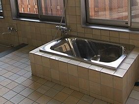 ステンレス製の浴槽が設置された浴室。ブラウンのタイル張りで、大きな窓が付いている。