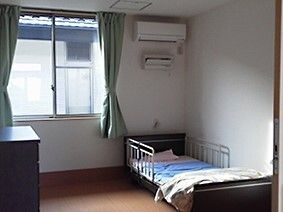 エアコンが付いた部屋には寝具付きのベッドが置かれ、大きな窓にはカーテンが付いている。