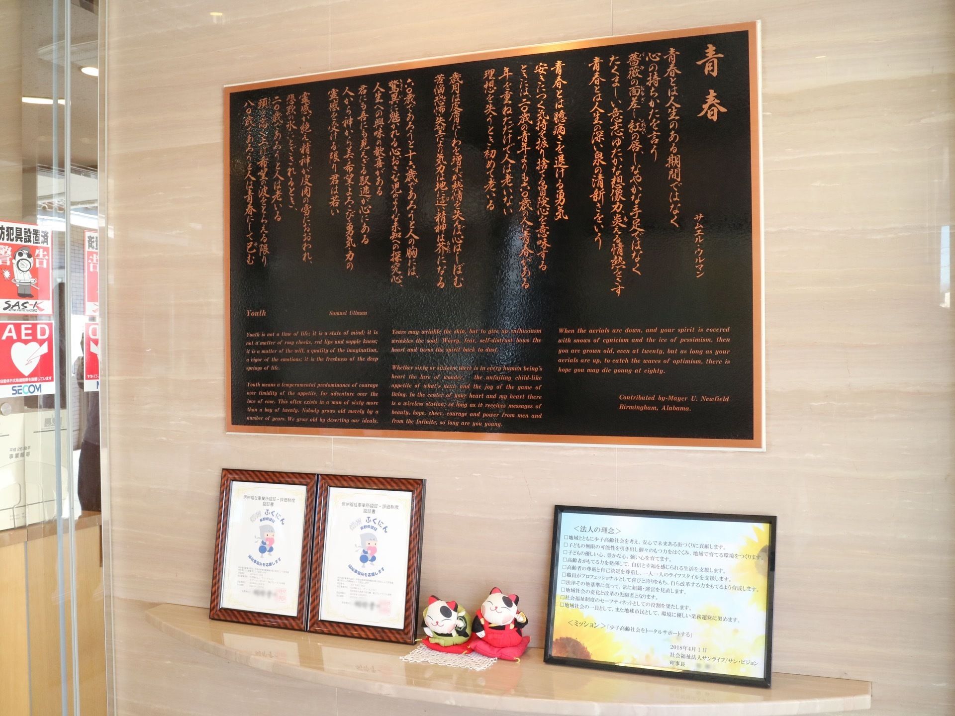 玄関の壁に運営法人の理念が書かれた紙が黒色の額縁に入れて置かれている。その横に、かわいい小動物の置き物が２つ並んでいる。