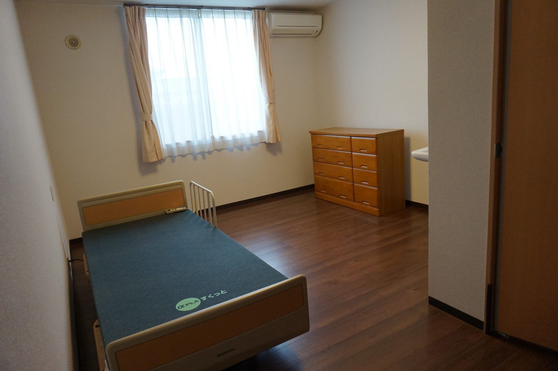 屋外で笑顔で過ごしている車いすの高齢女性と付き添いの若い女性スタッフ。日当たりのいい場所で。