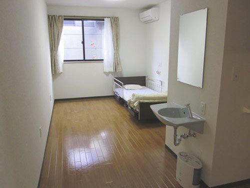 介護ベッドが置かれた部屋の壁に、エアコンと洗面台、鏡が設置されている。床の上に加湿器が備えられている。