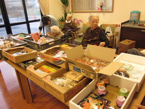 ダンボールに入ったパンや海苔のつくだ煮などの食料品が、机の上に並べられている。車椅子をご利用の方が選んでいる。