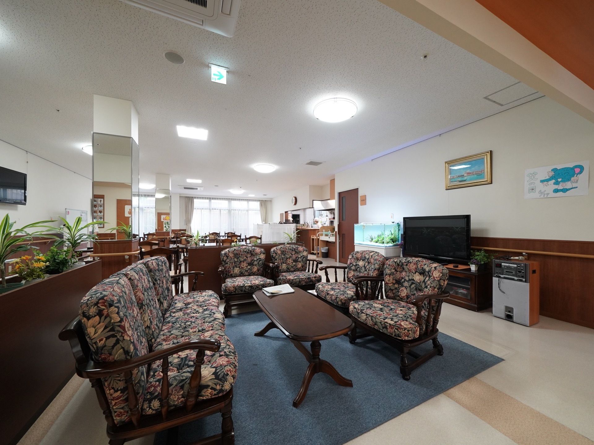 玄関ホールの真ん中あたりにグレーの絨毯が敷いてあり、その上にテーブルとソファーが置いてある。右側の壁には、絵が掛けてある。
