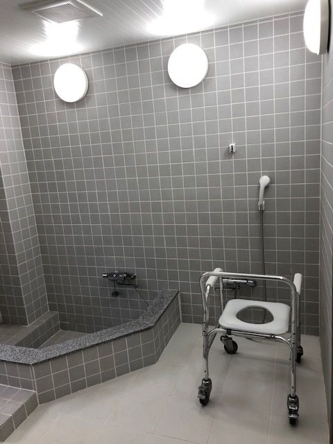 グレーのタイルが貼られた浴室には浅めの浴槽とコロ付きの浴室用チェア、シャワーがある。