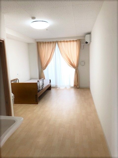 フローリングのシンプルな居室。カーテンが付けられた窓が大きく日当たりがいい。エアコン付き。