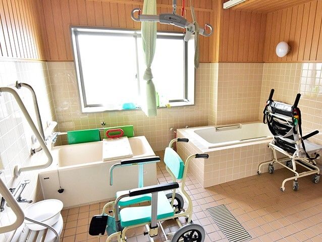 大きな窓が付いた浴室の左右に一人用の浴槽があり、中央にはカーテンがある。リフトやバスボード、シャワーなどがあり、手すりも付いている。