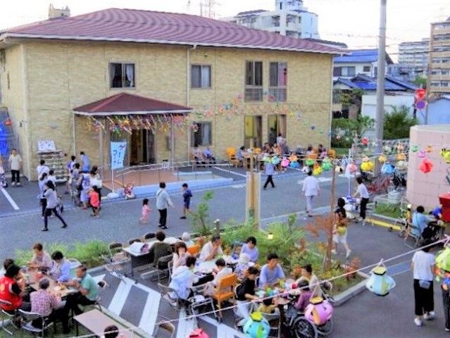 手作りのカラフルな提灯が飾られた建物の外のスペース。たくさんの人が行き来していて、テーブル席も用意されている。