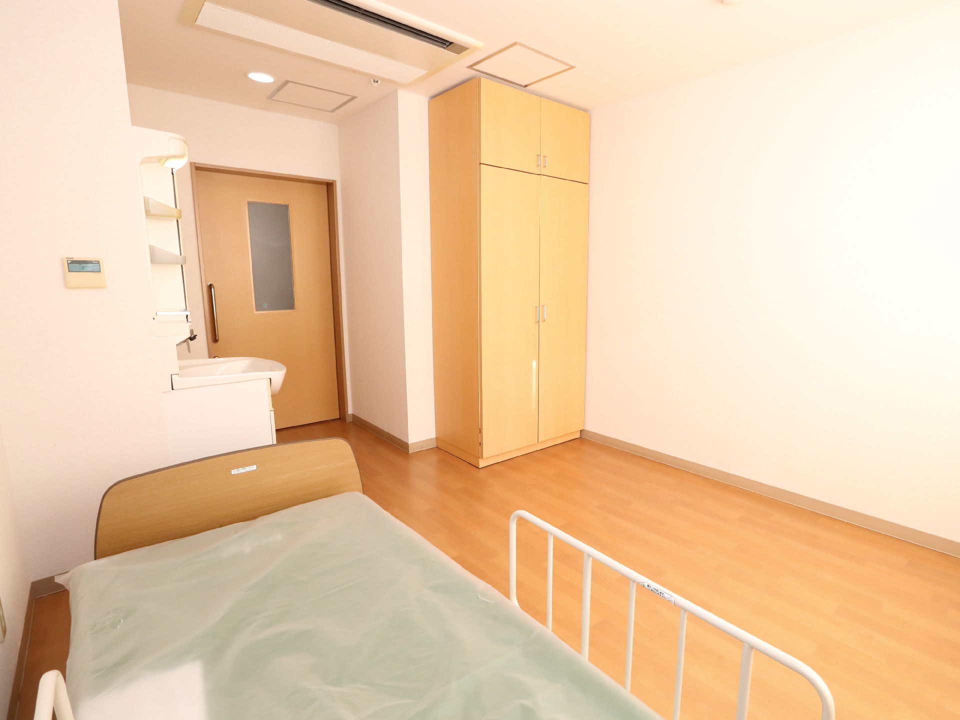 大きな窓が付いたフローリングの部屋。寝具付きのベッドが置かれ、デスクセットもある。