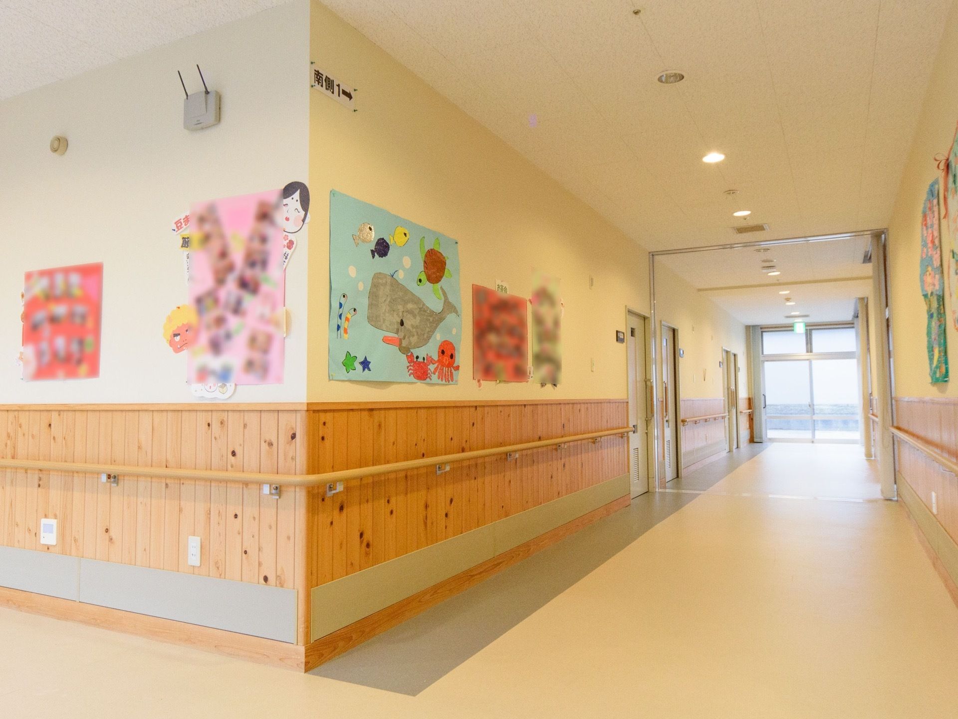 ゆとりある広々とした廊下で、床はフローリングとなっている。壁には絵やイベント時の写真が飾られている。