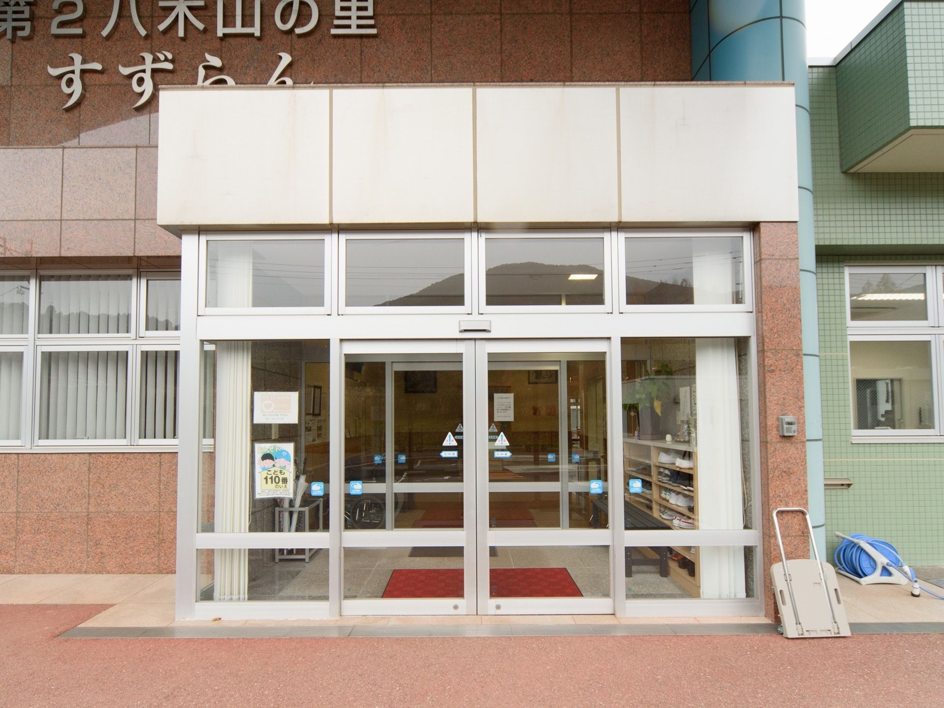 自動ドアが設置されている玄関で、ガラス張りとなっているので館内の様子がよく見える。ブラウンを基調とした外壁には施設名が書かれている。