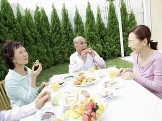 晴れた天気のもと、ご高齢な男女4名が食事をしながら親しげに会話をしている。