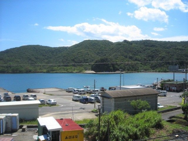 手前には港、その向こうには波のない穏やかな海と山が見える。