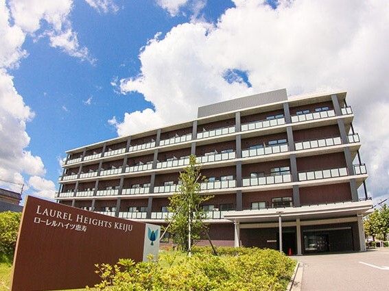 鉄骨造の建物の外観写真。手間にローレルハイツ恵寿の看板が出ている様子