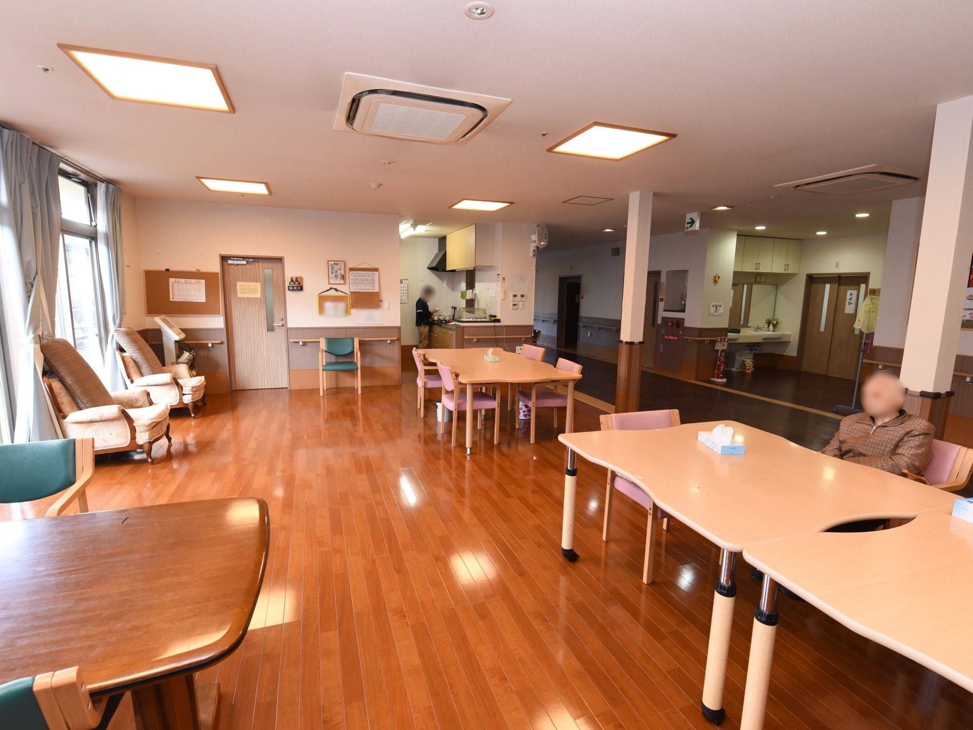 食堂は広々としており、複数のテーブル、椅子が置かれている。壁には手すりが設置されている。椅子には入居者様が座っている。