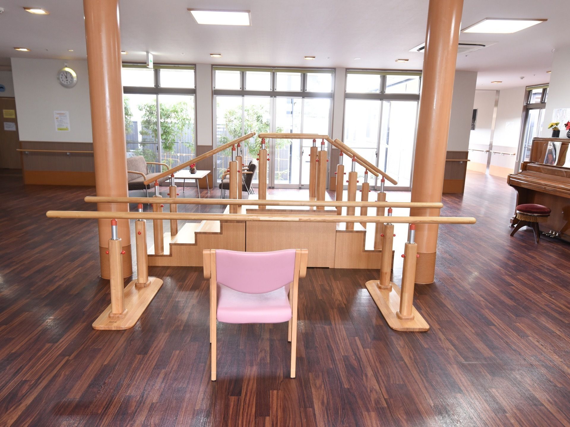 機能訓練室には木製のピアノと座面が円形の椅子がある。離れた場所には平行棒と歩行練習用階段が置かれている。