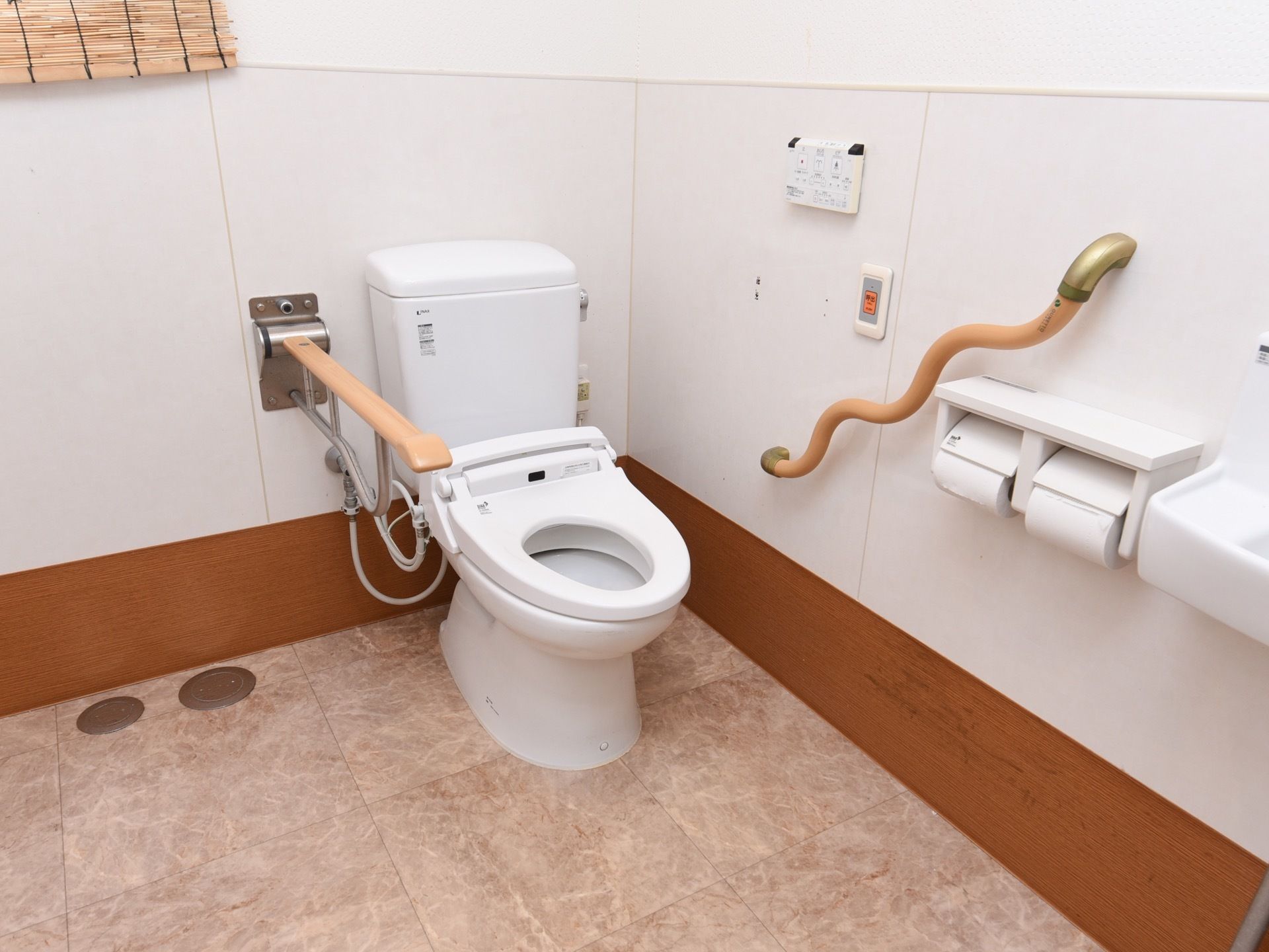 トイレには洋式便器が設置されている。壁には操作ボタンと呼び出しボタン、波波の形状の手すりが取りつけられている。