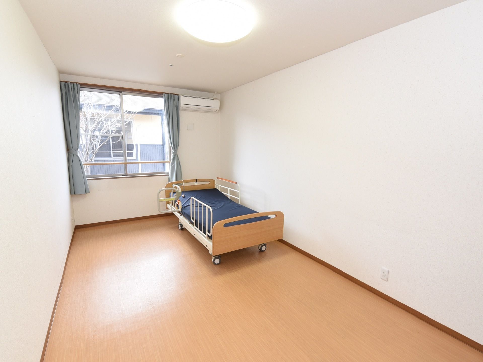 居室には、正面に窓があり壁面の上部にエアコンがついている。壁際には、安全性の高い介護用ベッドが備えつけられている。