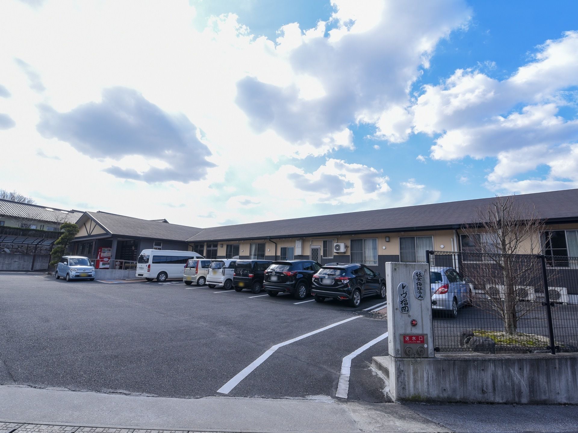 施設の門を入ると、コンクリート舗装された段差のない敷地が広がっている。平屋建ての施設前には、駐車場が完備され多数の車が並んでいる。