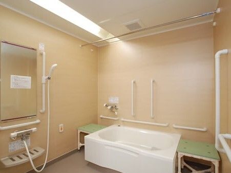 オレンジの呼び出しボタンが付いた一人用の浴室。シャワーや手すりが付き、洗い場も広く、明るい雰囲気。