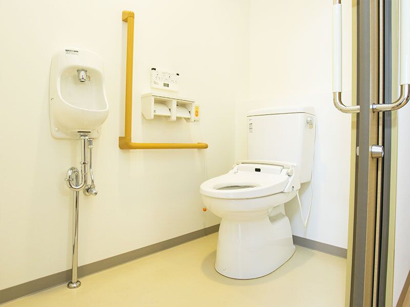 広いトイレにはエル字型の手すりやオレンジの呼び出しボタンが設置され、引き戸が付いている。