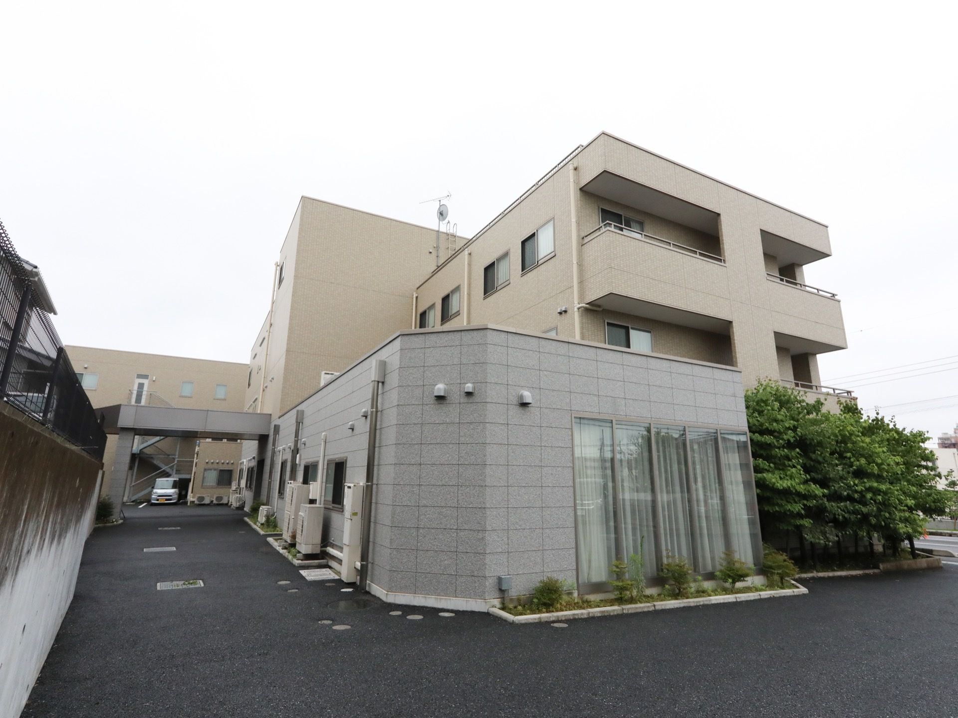 四角く、スタイリッシュな外観の施設。施設横には花壇があり、樹木が植えられている。ベランダがついた居室がある。