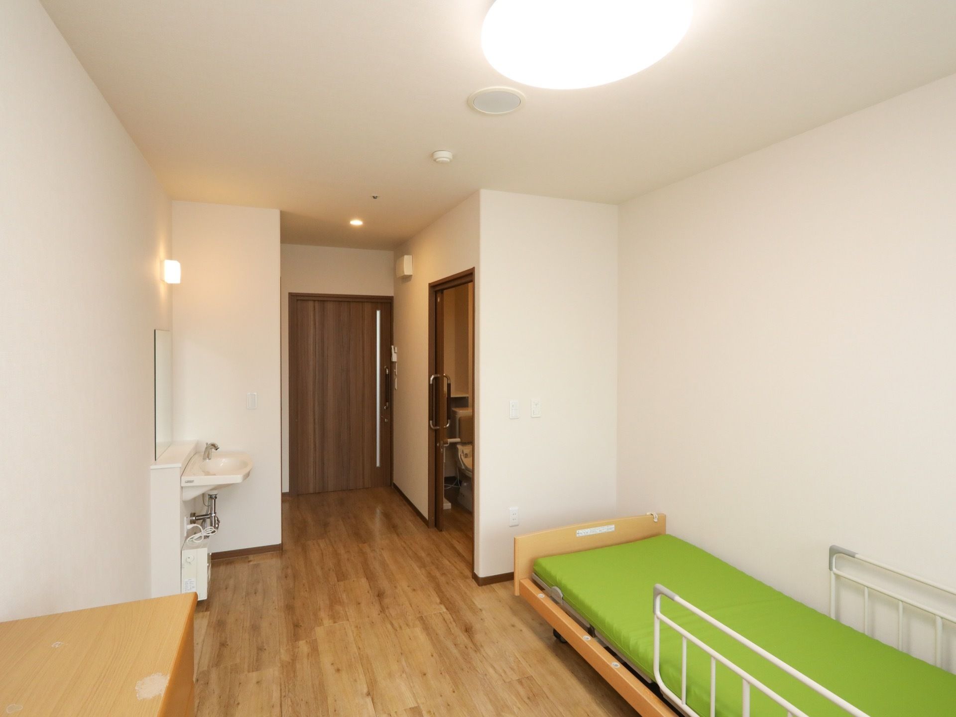 居室のドアは全てスライド式のドアとなっており、鏡付きの洗面台とトイレが備わっている。柵付きの介護用ベッドが置かれている。