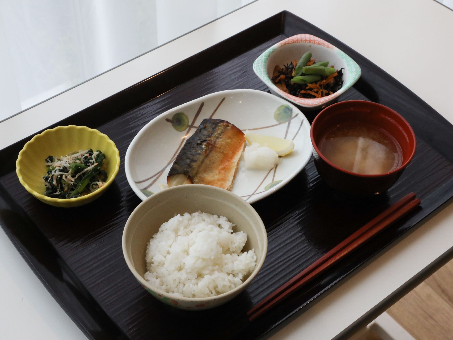 大根おろし付きの焼き魚と、小鉢に盛られたおかず２品、味噌汁、白いご飯が用意された食事