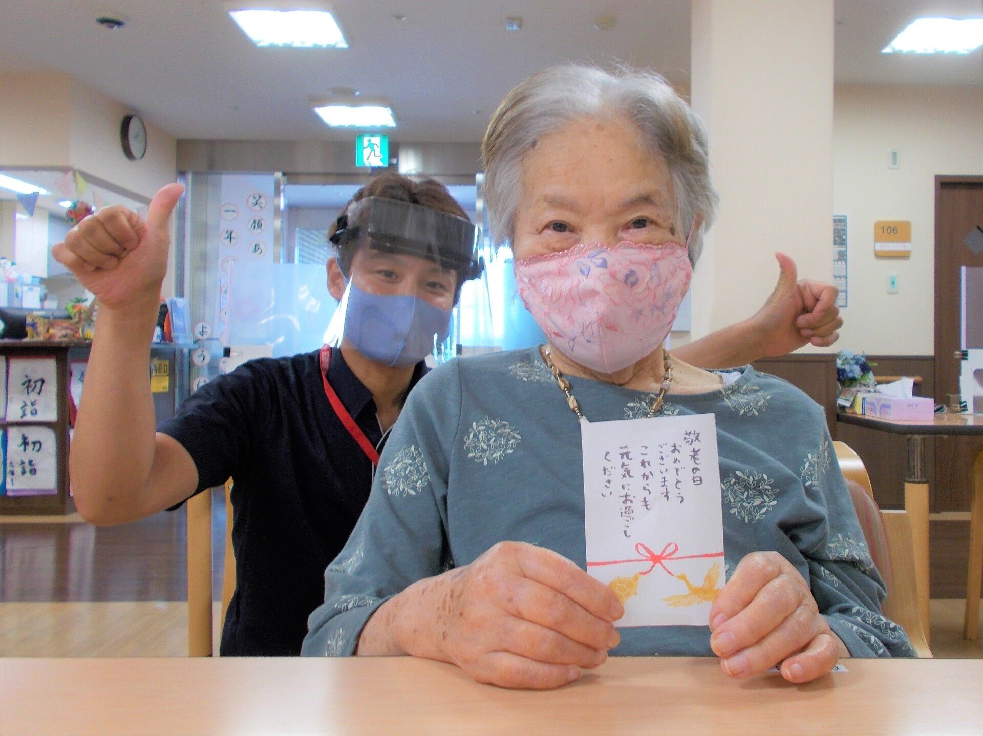 眼鏡をかけた高齢男性が車から降りようとしているところを、手を差し伸べ介助しているエプロンを付けたスタッフ。
