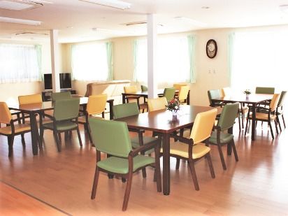 肘置きが付いたカラフルな椅子がセットされたダイニングテーブルが複数置かれた食堂。