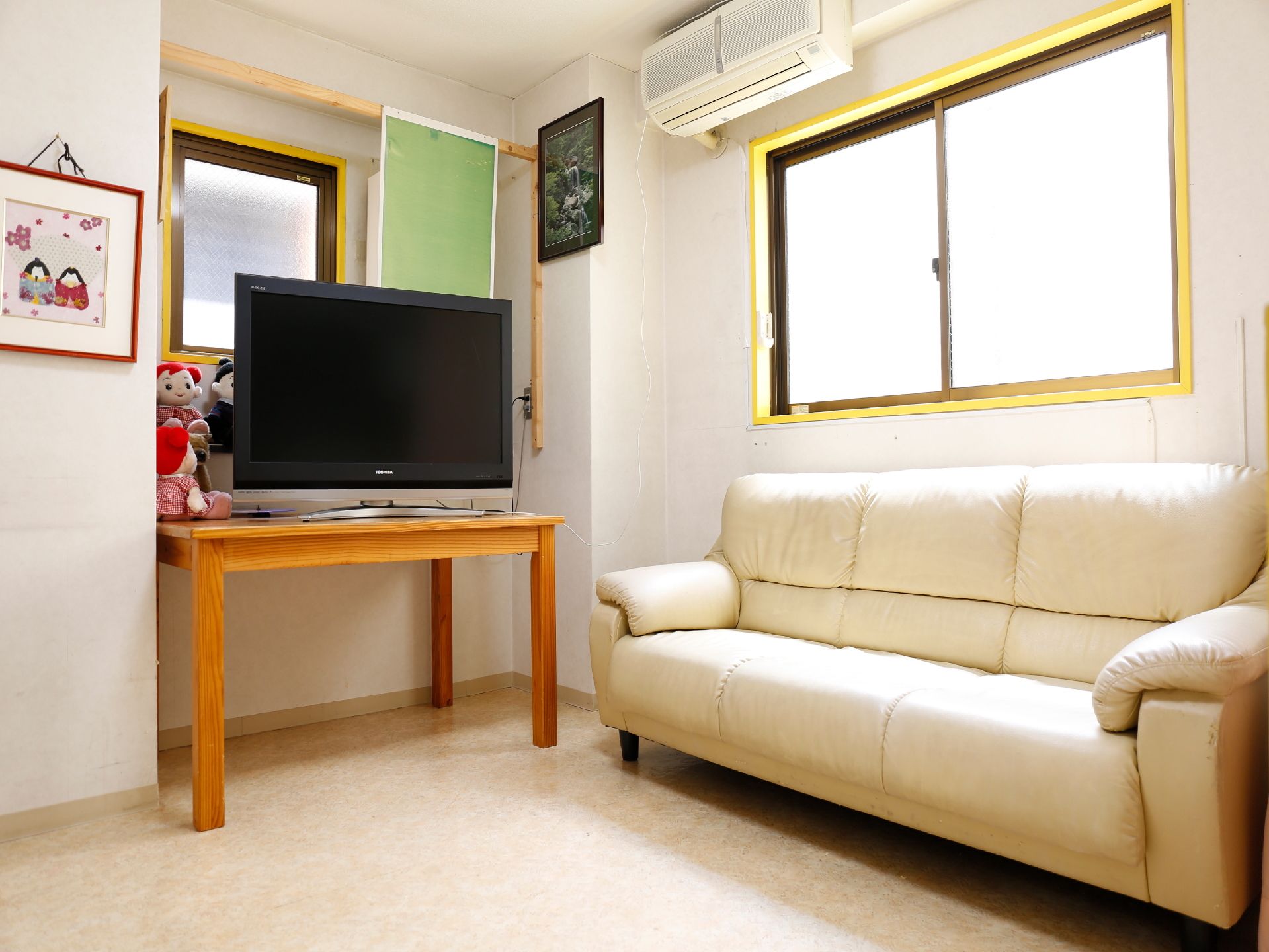 部屋の角にふかふかの大きなソファーがある。横にはテーブルがあり、上に大きなテレビが乗っている。ソファーの上側には窓がある。
