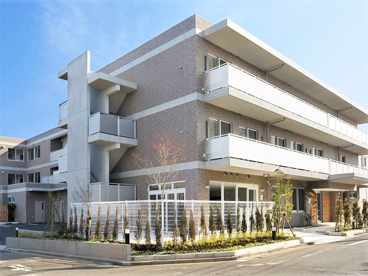 通常のマンション風の建物の外観。３階建ての建物に日がさしている様子