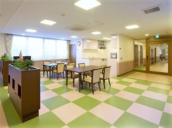 市松模様の床が印象的な施設内の緑道。シックなこい茶色tの椅子、テーブルが並んでいる様子