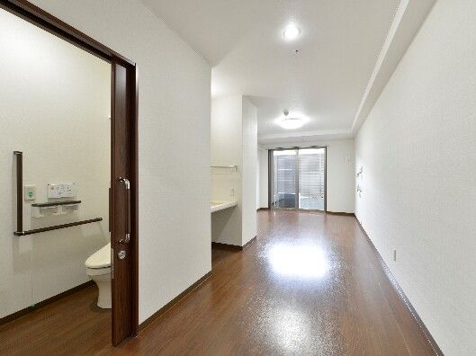 フローリングの部屋。手すりや呼び出しボタンが付いた広いトイレにはスライド式のドアが設置されている。
