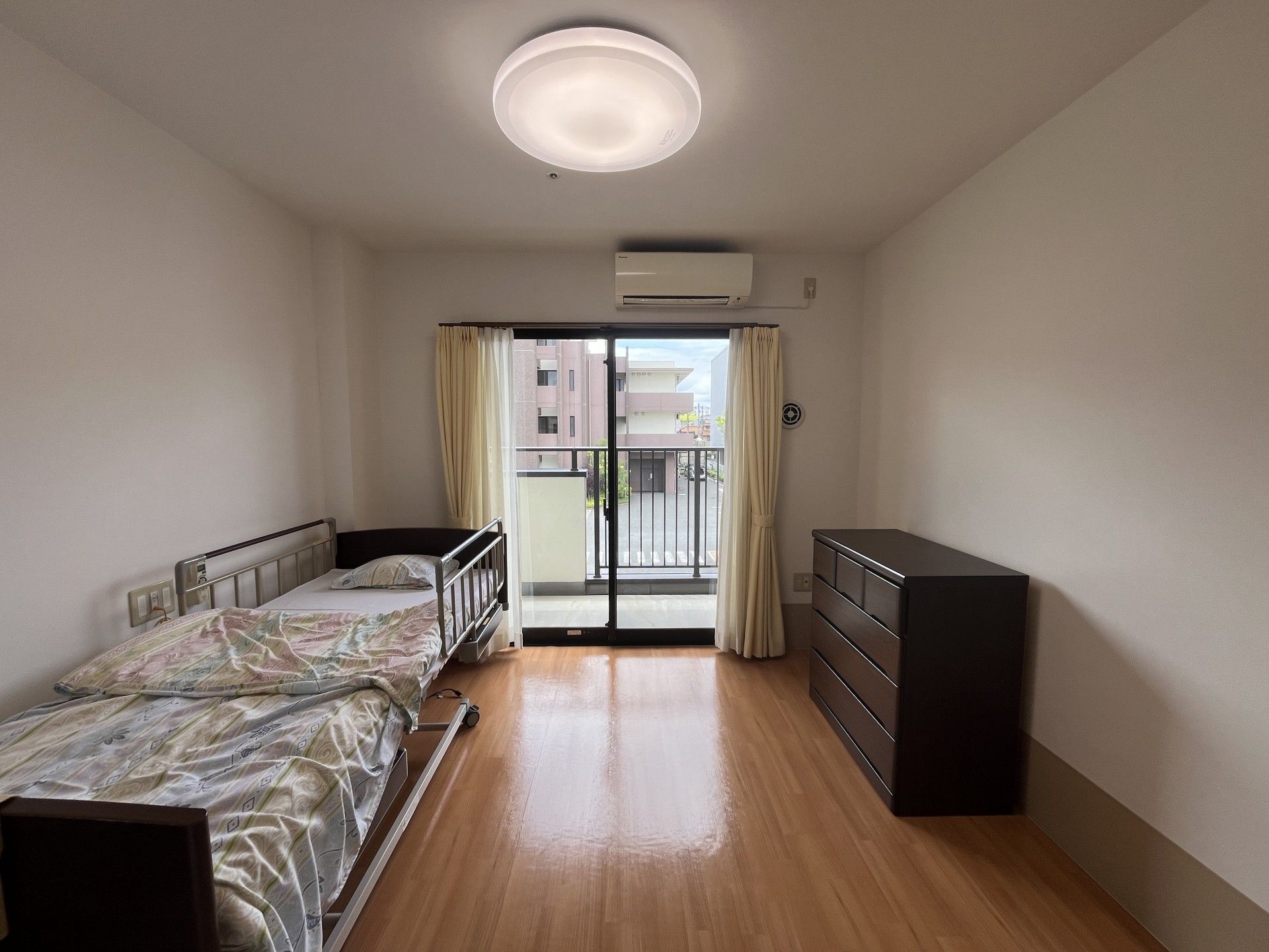 自然豊かな場所を車いすで散歩している高齢男性とそれを補助しながら話している女性スタッフ