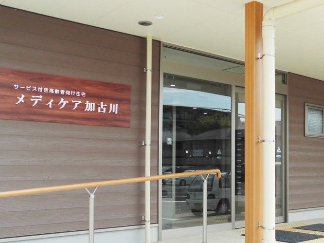 玄関の外壁には住宅名が掲げられ、ドアを出るとすぐ手すり付きのスロープがついている。