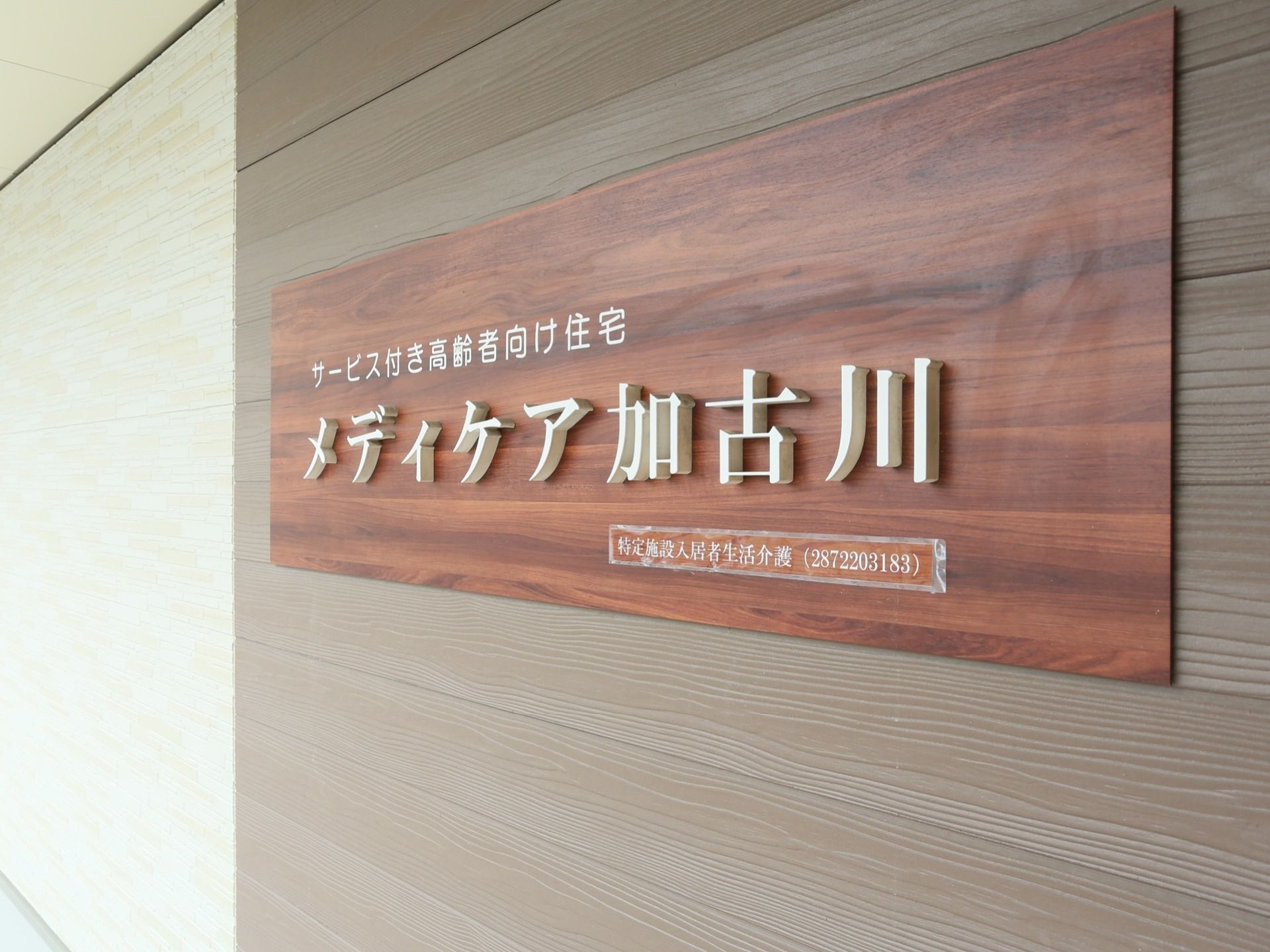 木目調の壁の前にある木製の看板に、立体的な文字プレートで施設名が記されている。落ち着いた雰囲気の外装である。