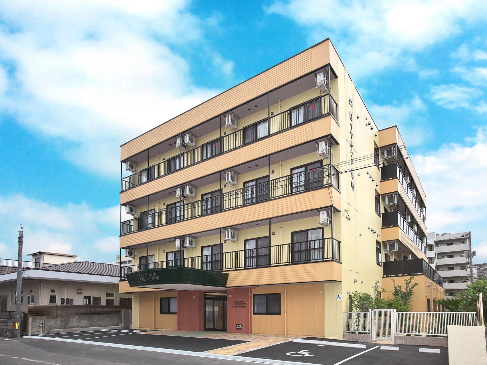 各フロアにベランダがあるベージュの外壁の４階建ての建物。周辺に背の高い建物がなく、日当たり良好。
