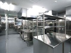 本格的なステンレス製の調理器具や大きな作業台が置かれた厨房。きれいに片付けられている。