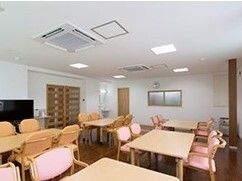 ピンクやオレンジの椅子がセットされたテーブルが複数並んでいる食堂。テレビが設置されたスペースもある。