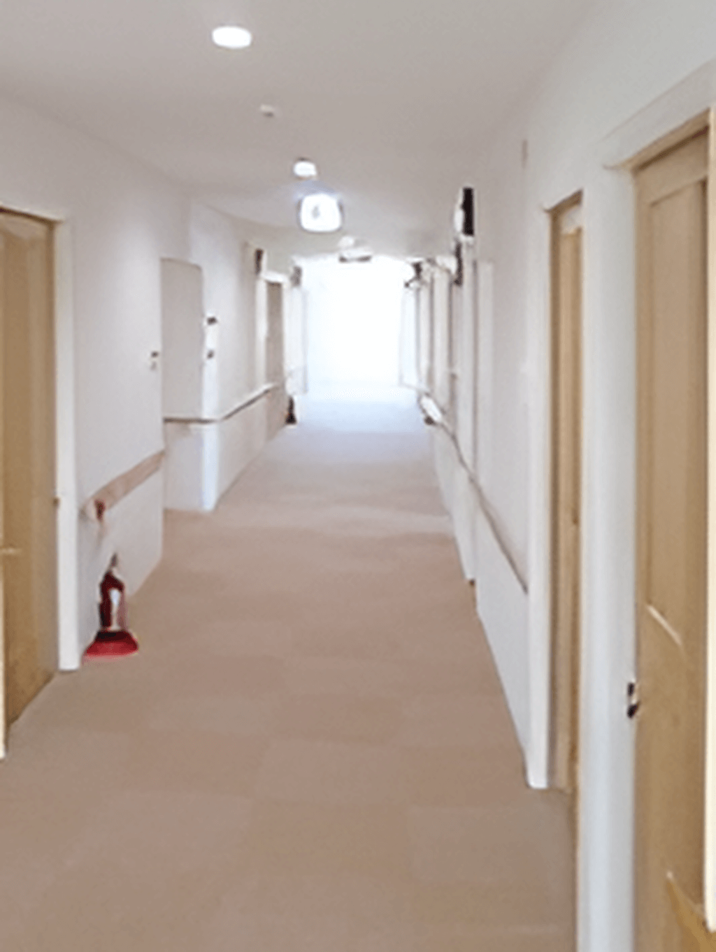 まっすぐな廊下の両サイドに手すりと居室のドアが並んでいて左側には消火器も置かれている。