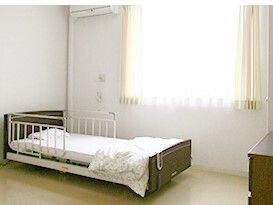 大きな窓が付いた明るい雰囲気の部屋にはエアコンが付き、寝具付きのベッドが置かれ、タンスのようなものもある。