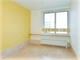シンプルなフローリングの居室は窓が大きく、壁の一面が黄色、手すりもついている。