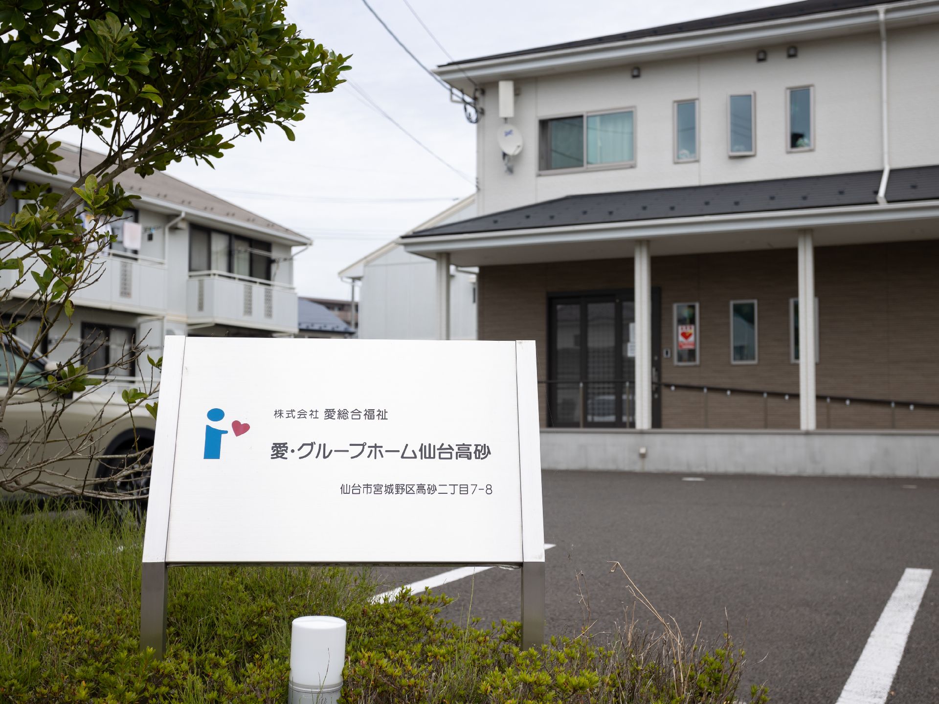 白とブラウンの外観の建物の前に立っている銀色の看板