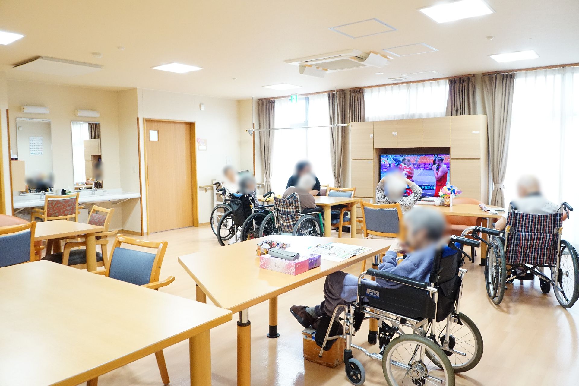 大きなガラス戸があり、テレビの回りに入居者が集まっているリビング