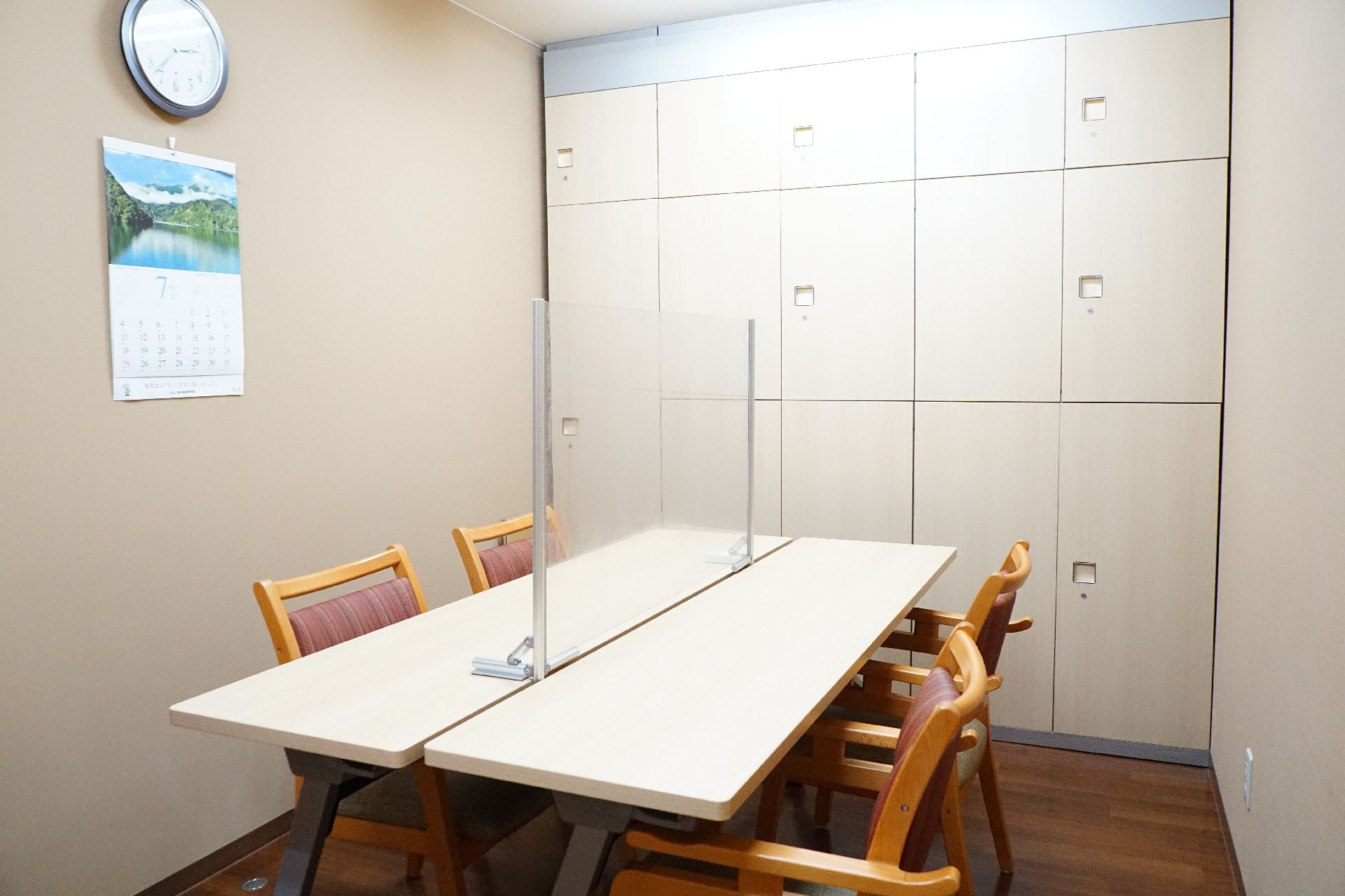 テーブルを挟んで椅子が設置され、時計、カレンダーが置かれている共有スペース