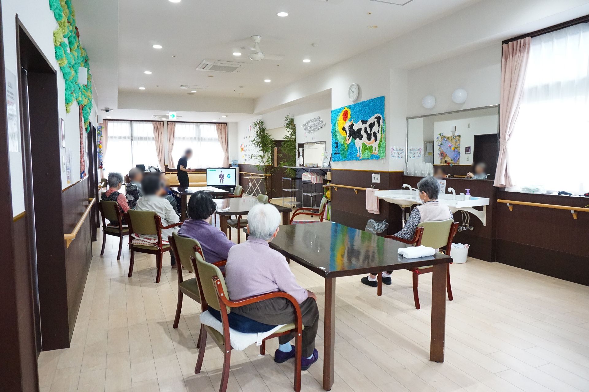 窓から陽光が入り、椅子に座って入居者がテレビを見ているリビング