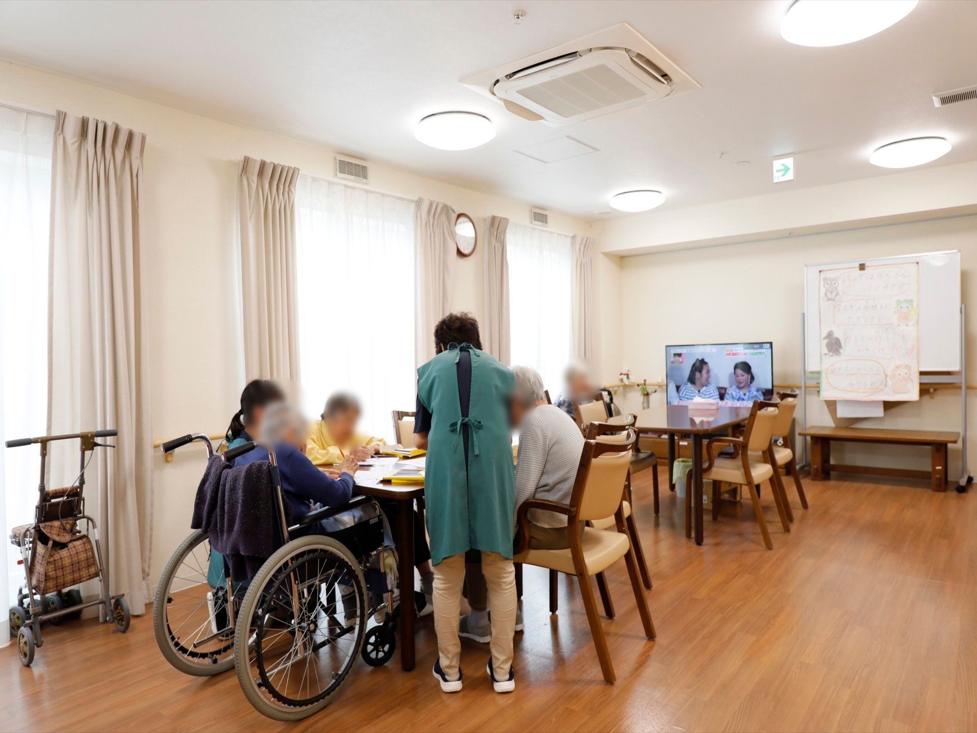 設置されたテレビが点灯し、横のホワイトボードの下に木製ベンチが置かれた共有スペース