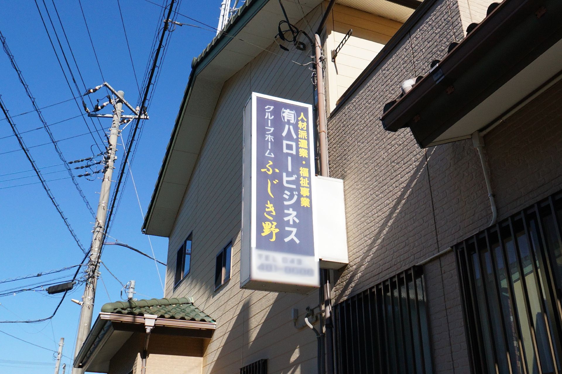 机の上にはアジサイの貼り絵が置かれていて、エプロンを付けた若い女性スタッフと黒髪の高齢女性が楽しそうに取り組んでいる様子。